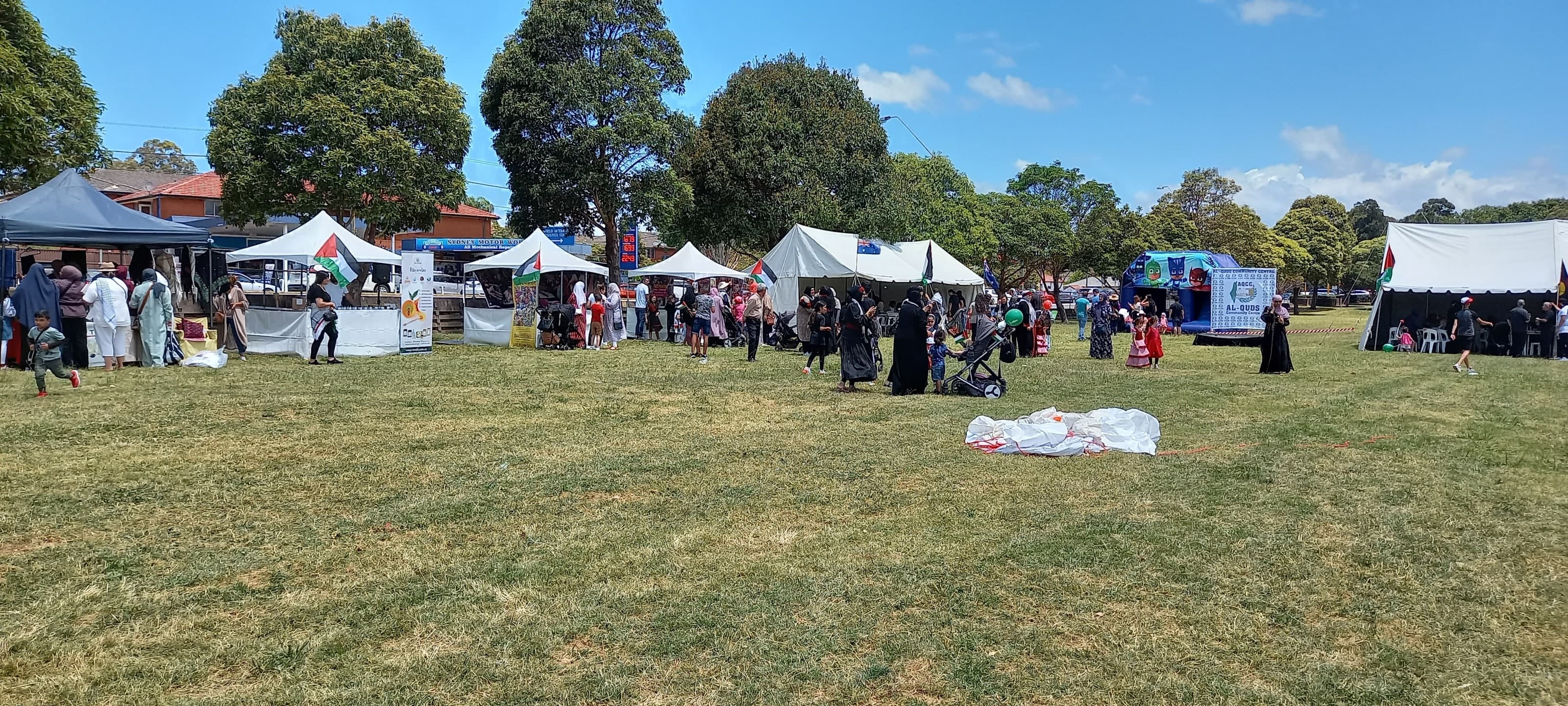 Families walking between the white stall tents on the grass, with Palestinian flags flying