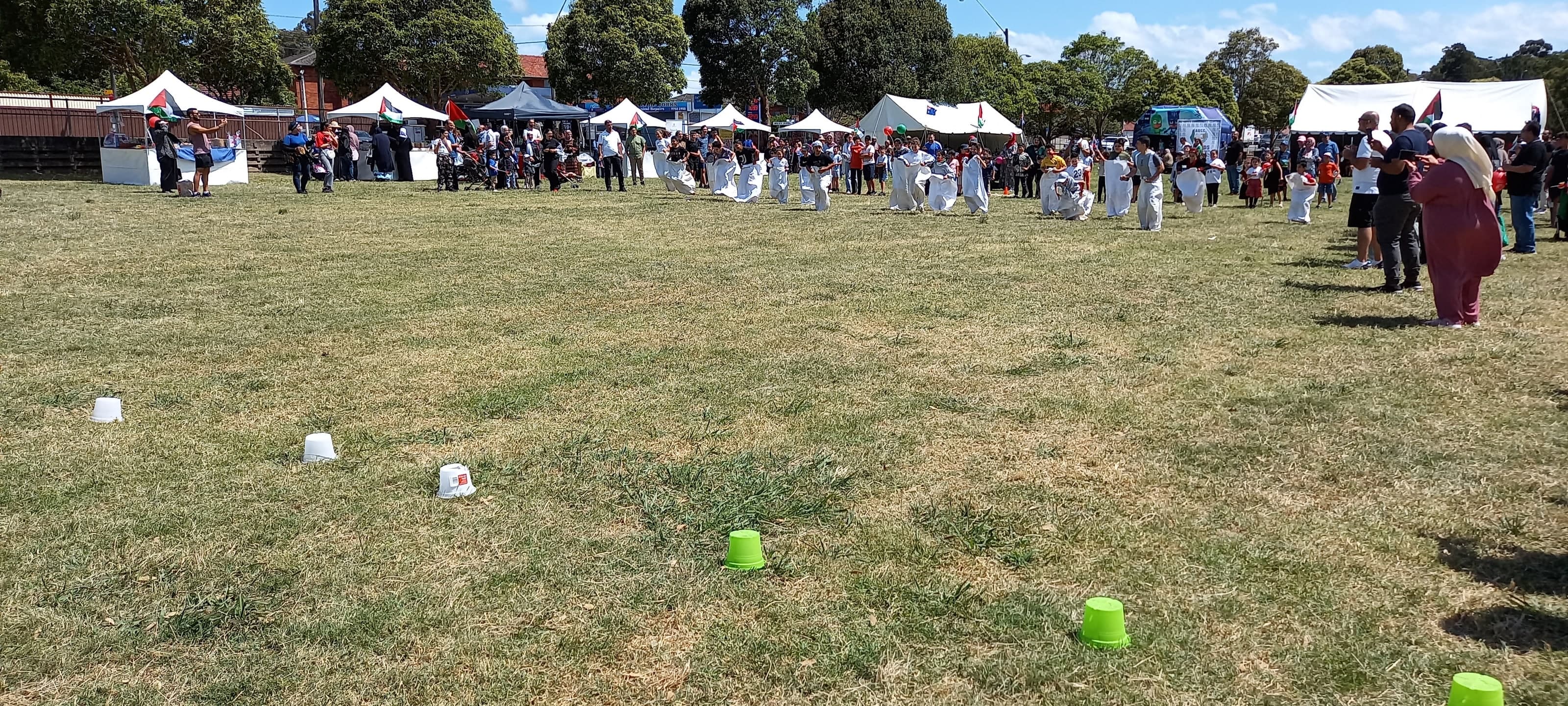 Children in sacks setting off across the field, watched by a crowd in front of the tents