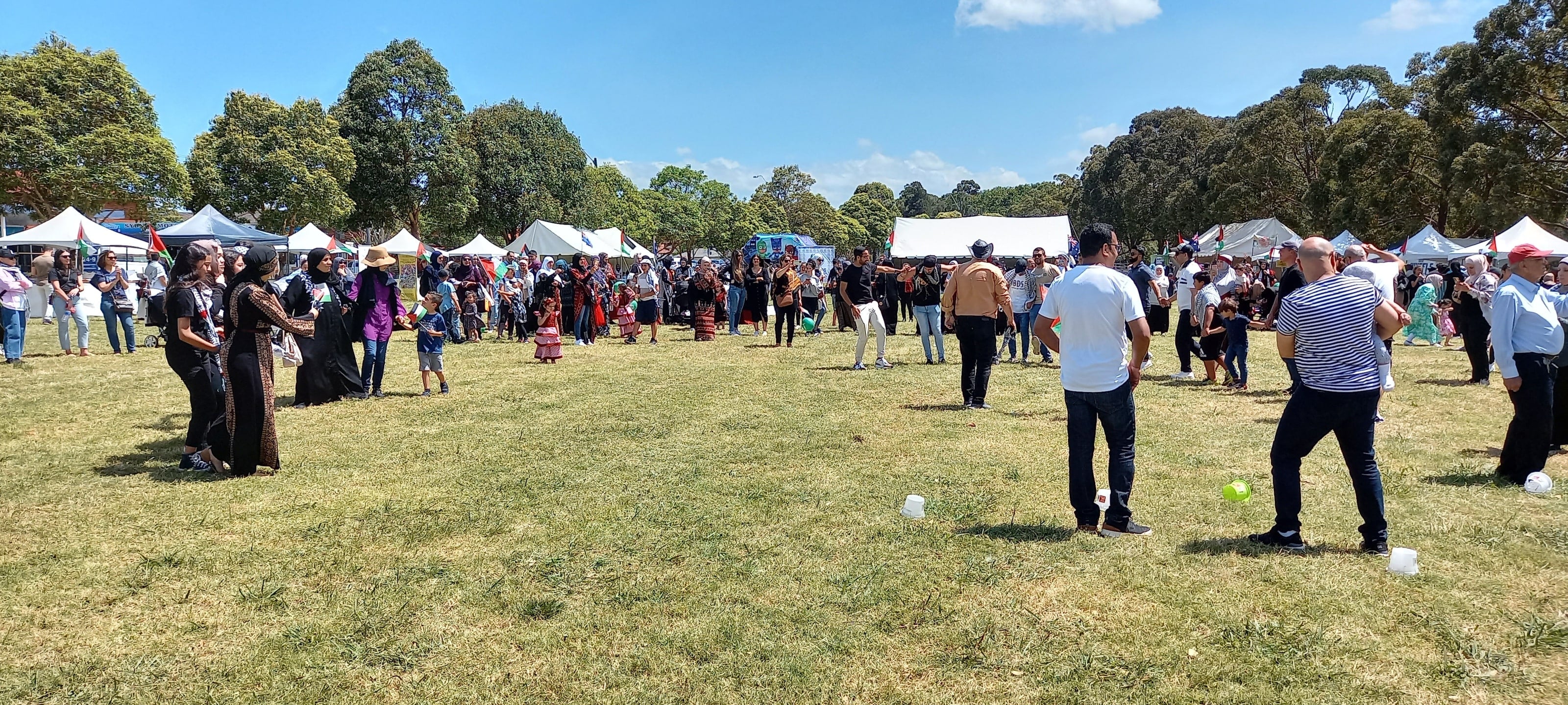 A crowd in Palestinian dress gathering in a wide circle on the field as the dabka starts