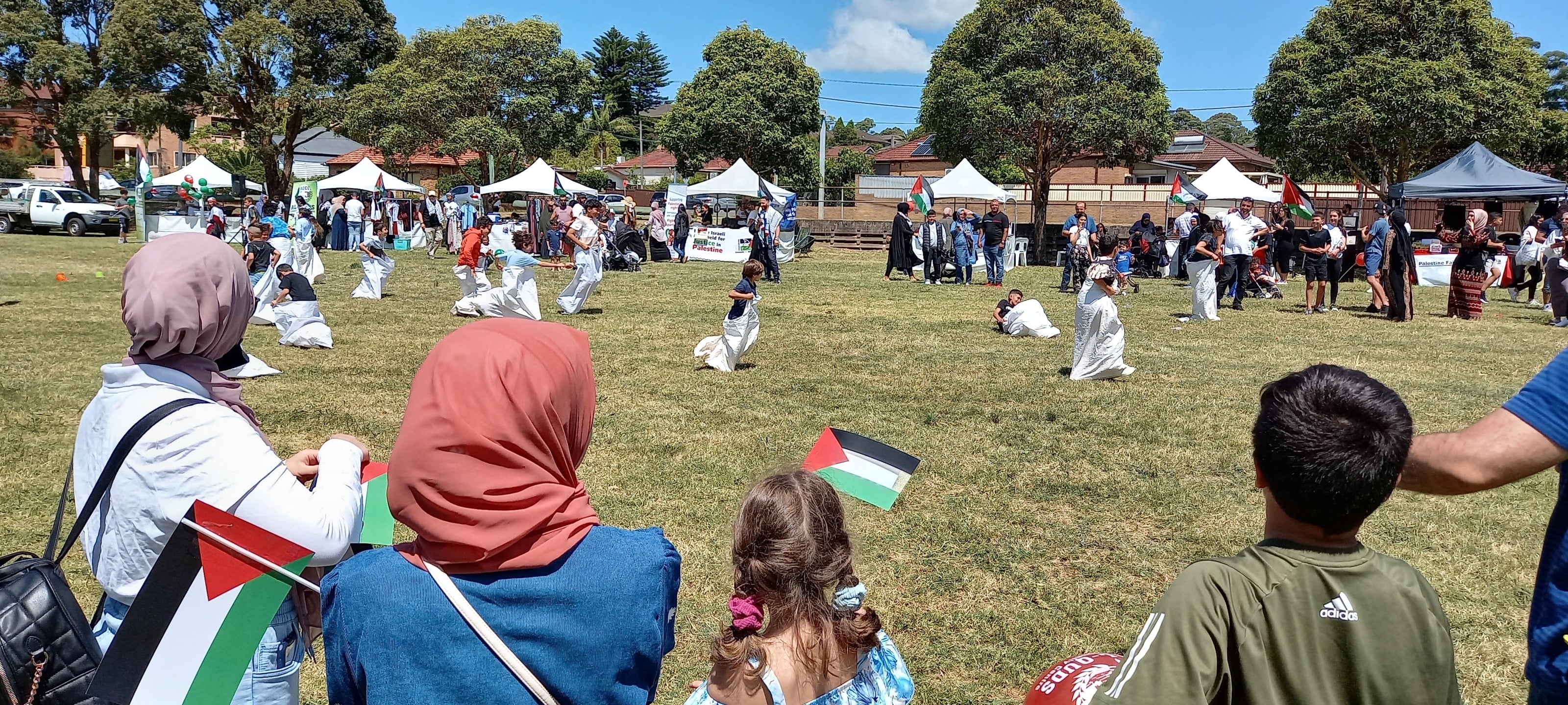 Children hopping in sacks while families watch, holding small Palestinian flags