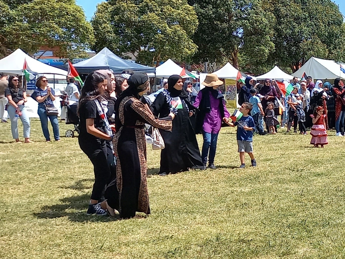 A crowd in Palestinian dress gathering in a wide circle on the field as the dabka starts